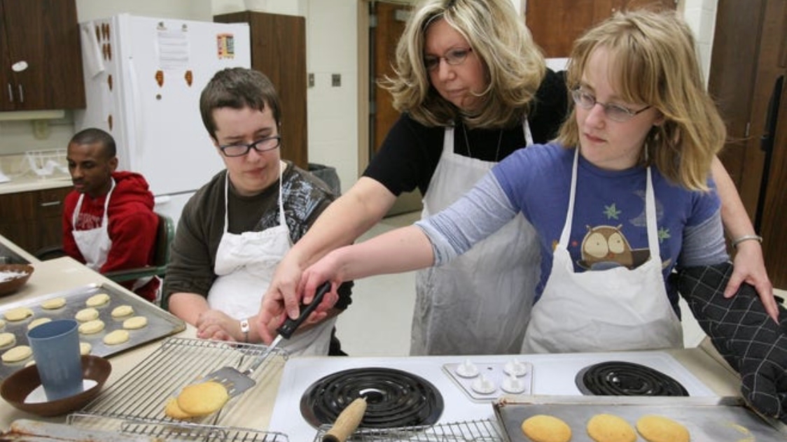 Pictured are 3 students baking cookies in class with their Teacher