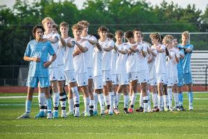 high school boys soccer team lined up with hands on eachother's shoulders for the national anthem